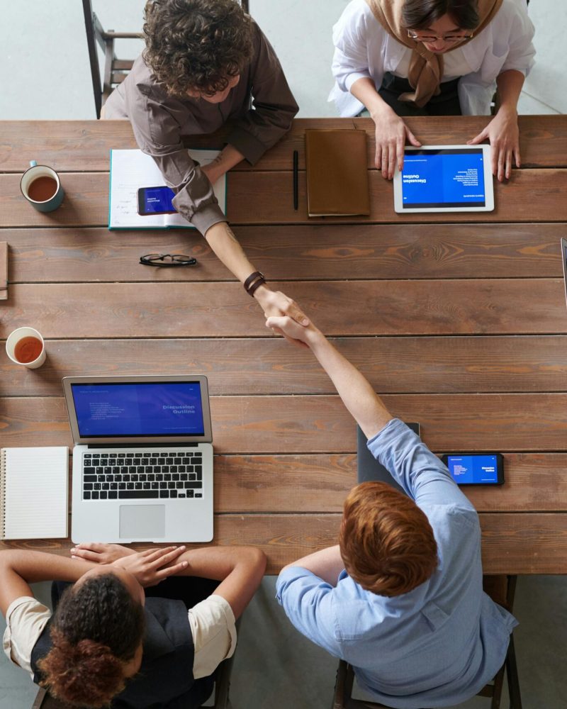 Overhead view of colleagues in a work meeting using laptops and tablets, emphasizing teamwork and technology.