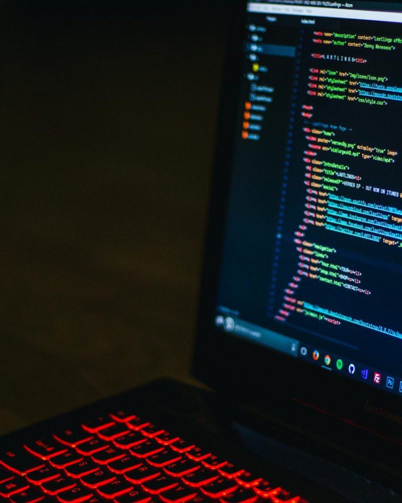 Red backlit keyboard and code on laptop screen create a tech-focused ambiance.